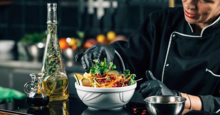 Chef in a restaurant kitchen decorating an innovative vegan dish with parsley