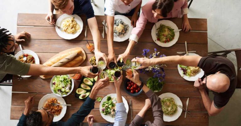 Diverse group of restaurant guests toasting with drinks at a table serving an inclusive menu of pasta and vegan dishes