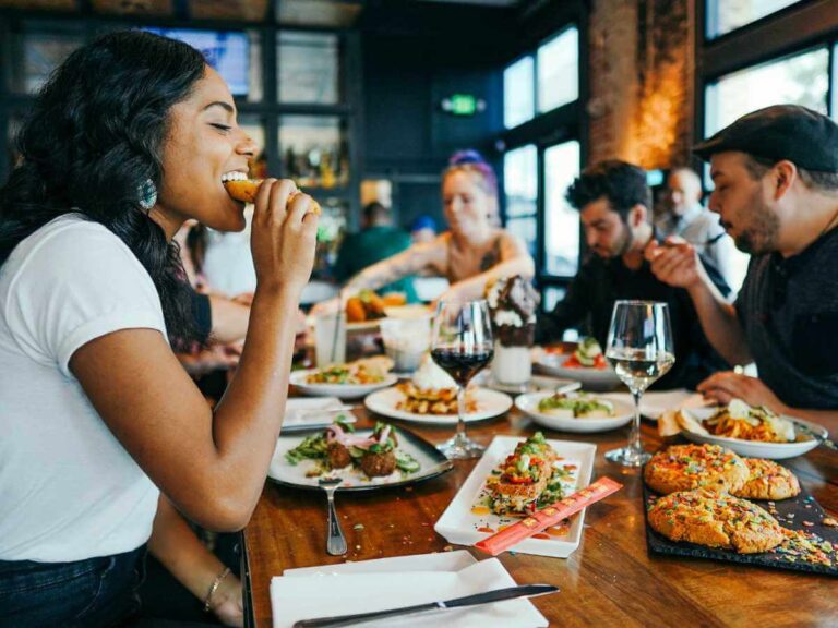 Woman and her friends sitting at a restaurant table with food and wine enjoying a variety of vegan food