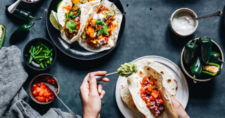 Someone in the kitchen cooking delicious vegan tacos with guacamole, tomatoes, and corn