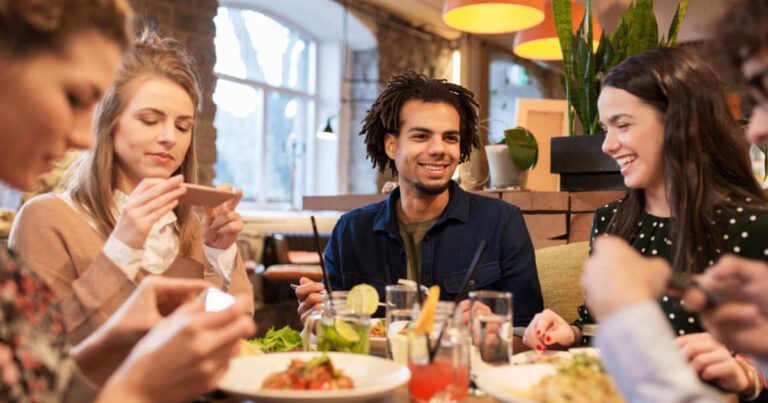 A group of friends enjoying vegan food at a restaurant and taking pictures of their dishes to post on social media