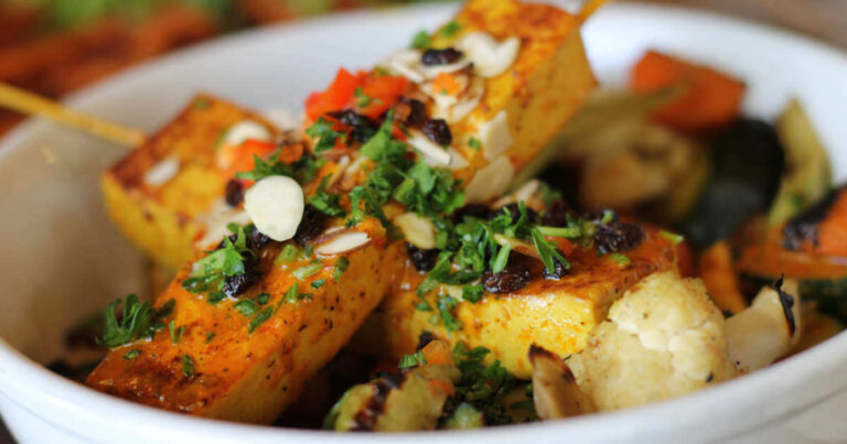 A beautifully plated vegan dish with tofu and grilled vegetables, garnished with parsley and almonds