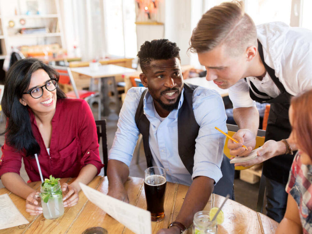 A group of friends ordering food at a restaurant and asking questions about the menu to the waiter