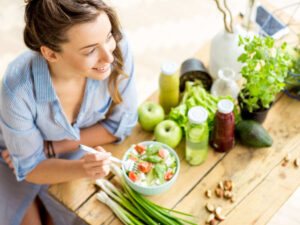 A woman eating a healthy vegan salad with tofu and nuts at a table decorated with fresh vegetables and fruit