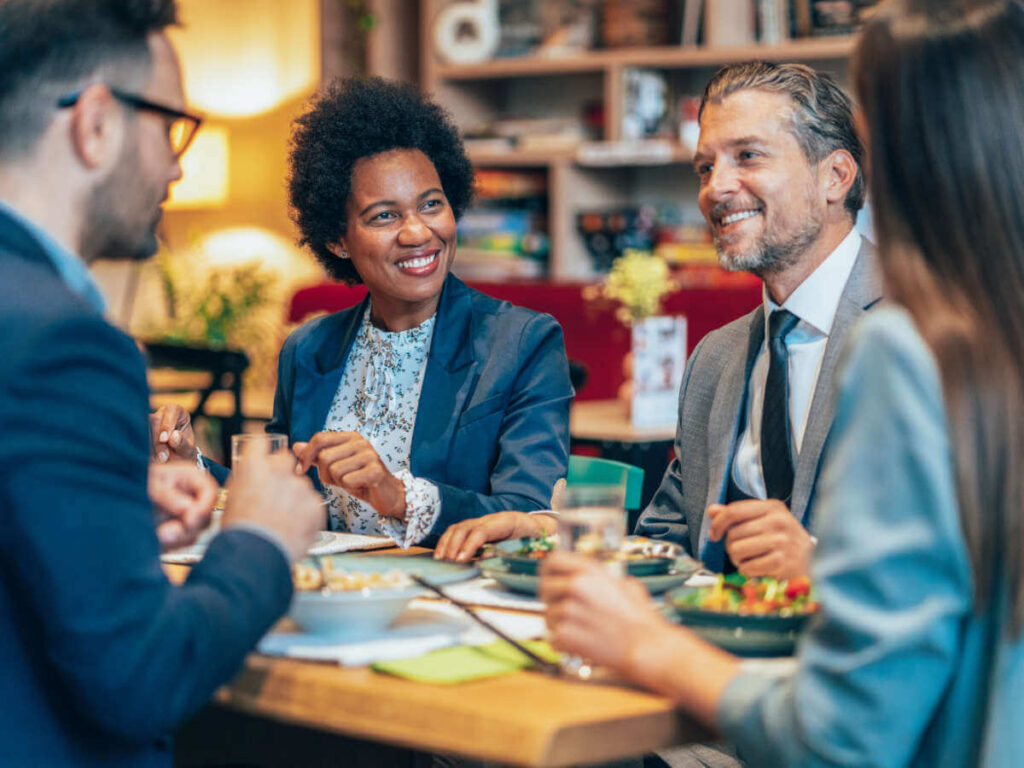 A group of co-workers smiling while eating a healthy vegan lunch at the office canteen