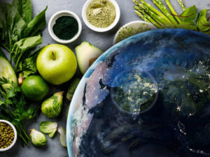 Satellite image of Earth in front of a variety of green vegan food, including apple, avocado, live, spinach, and lentils