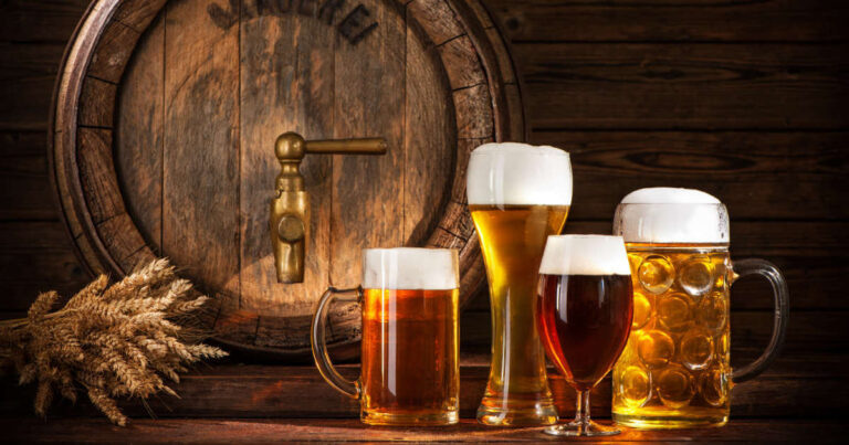 Four different clarified beers in glasses standing in front of a brewing barrel